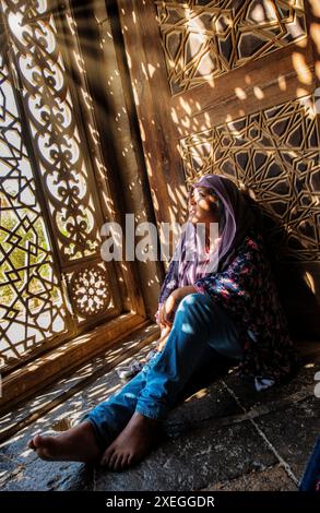 Amira illuminata dai raggi del sole che splendono attraverso gli schermi decorativi a reticolo della Moschea al-Rifai Foto Stock