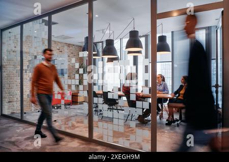 Nel caos dinamico di un ambiente di lavoro, un gruppo di giovani professionisti percorre il corridoio successivo Foto Stock