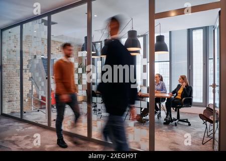 Nel caos dinamico di un ambiente di lavoro, un gruppo di giovani professionisti percorre il corridoio successivo Foto Stock