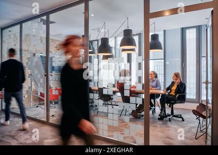 Nel caos dinamico di un ambiente di lavoro, un gruppo di giovani professionisti percorre il corridoio successivo Foto Stock