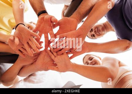 Giovani sorridenti in abbigliamento sportivo che mettono le mani insieme su uno sfondo chiaro. Donne e uomini in piedi in cerchio e che si tengono per mano Foto Stock