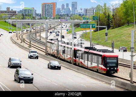 Calgary, Alberta Canada, 5 giugno 2024: Il trasporto pubblico su rotaia percorre la mediana centrale lungo il sentiero Crowchild che si affaccia sullo skyline del centro. Foto Stock