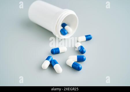 Capsule blu e bianche fuoriuscite da un vaso medicinali su sfondo blu. Foto Stock