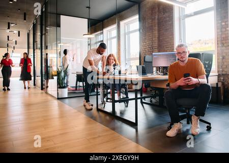 Un gruppo eterogeneo di professionisti collabora in un moderno centro di coworking startup, utilizzando un mix di supporti cartacei e. Foto Stock