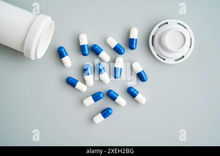 Capsule blu e bianche fuoriuscite da un vaso medicinali su sfondo blu. Foto Stock