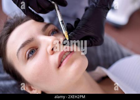 Iniezioni di bellezza. Cosmetologa donna in guanti neri fa un'iniezione Foto Stock