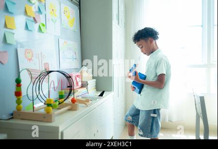 Piccolo artista che suona l'ukulele nel retro dell'aula, mentre aspetta che gli amici entrino in classe Foto Stock