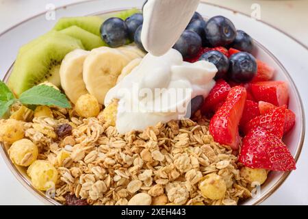 Muesli con fragole, kiwi, banana e mirtilli in un piatto rotondo con yogurt sul tavolo. Cibo sano e gustoso Foto Stock