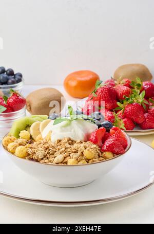 Muesli con fragole, kiwi, banana e mirtilli in un piatto rotondo con yogurt sul tavolo. Foto Stock