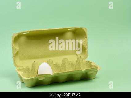 Un uovo bianco in una scatola di carta su sfondo verde Foto Stock