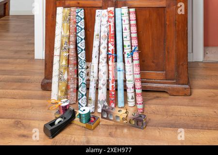 Un set di coloratissimi rotoli di carta per il natale e accessori per l'imballaggio regalo posizionati su un pavimento in legno Foto Stock