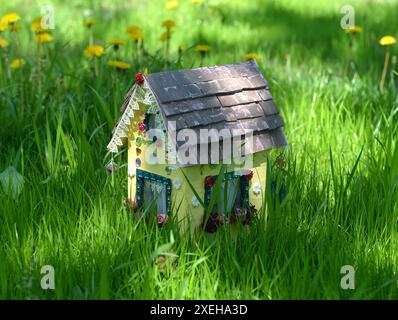 Adorabile casa di bambole sullo sfondo dell'erba all'aperto in estate o in primavera. Un'incantevole miniatura per biglietti d'auguri, matrimoni o compleanni Foto Stock