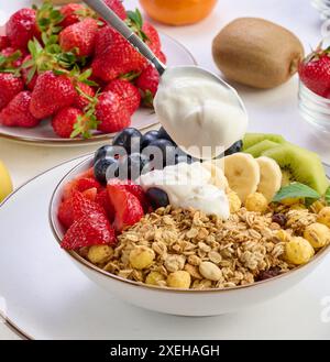 Muesli con fragole, kiwi, banana e mirtilli in un piatto rotondo con yogurt sul tavolo. Cibo sano e gustoso Foto Stock