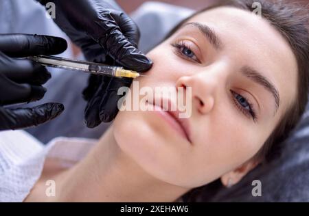 Iniezioni di bellezza. Cosmetologa donna in guanti neri fa un'iniezione Foto Stock