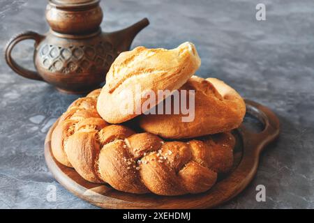 Diversi tipi di pane - kalacha, hala - pane intrecciato con sale grossolano. Pane sul tavolo con bollitore e caraffa, preparato per il consumo. Assortimento di Foto Stock