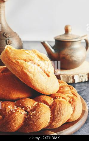 Diversi tipi di pane - kalacha, hala - pane intrecciato con sale grossolano. Pane sul tavolo con bollitore e caraffa, preparato per il consumo. Assortimento di Foto Stock