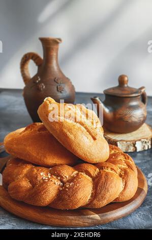 Diversi tipi di pane - kalacha, hala - pane intrecciato con sale grossolano. Pane sul tavolo con bollitore e caraffa, preparato per il consumo. Assortimento di Foto Stock