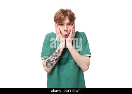 Giovane con i capelli rossi vestito con una t-shirt verde che tiene la testa di sorpresa Foto Stock