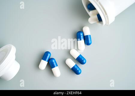 Capsule blu e bianche fuoriuscite da un vaso medicinali su sfondo blu. Foto Stock