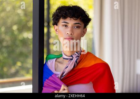 Indossando la bandiera dell'orgoglio, donna transgender in piedi in tutta sicurezza in salotto Foto Stock