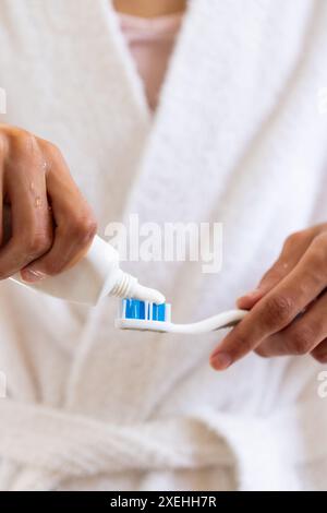 Applicazione del dentifricio sullo spazzolino da denti, giovane uomo in accappatoio per prepararsi a lavarsi i denti Foto Stock