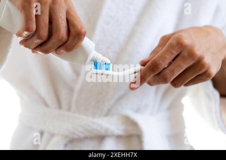 Applicazione del dentifricio sullo spazzolino da denti, giovane uomo in accappatoio per prepararsi a lavarsi i denti Foto Stock