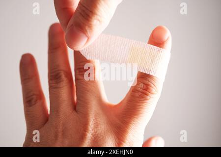 Applicazione di un cerotto adesivo a un dito. Primo piano. Foto Stock