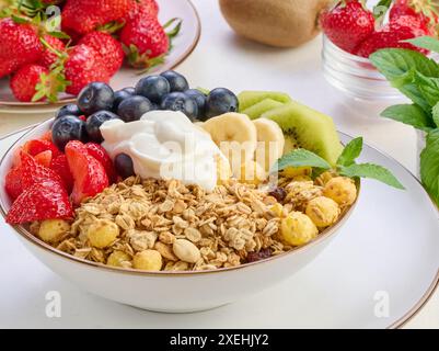 Muesli con fragole, kiwi, banana e mirtilli in un piatto rotondo con yogurt sul tavolo. Cibo sano e gustoso Foto Stock