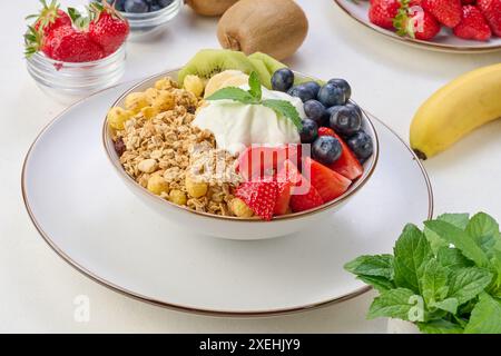 Granola con fragole, kiwi, banana e mirtilli in un piatto rotondo su un tavolo bianco. Foto Stock