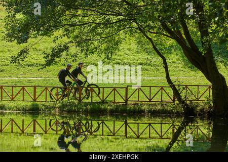 Una coppia beata, adornata di attrezzatura da ciclismo professionale, gode di una romantica corsa in bicicletta attraverso un parco, circondato dalla moderna nat Foto Stock