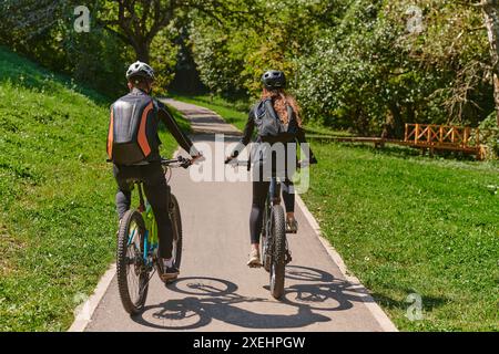 Una coppia beata, adornata di attrezzatura da ciclismo professionale, gode di una romantica corsa in bicicletta attraverso un parco, circondato dalla moderna nat Foto Stock