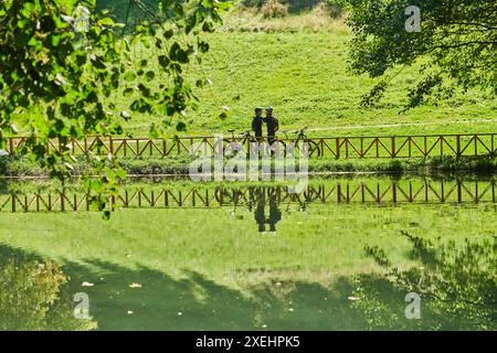 Una coppia beata, adornata di attrezzatura da ciclismo professionale, gode di una romantica corsa in bicicletta attraverso un parco, circondato dalla moderna nat Foto Stock