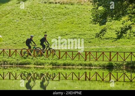 Una coppia beata, adornata di attrezzatura da ciclismo professionale, gode di una romantica corsa in bicicletta attraverso un parco, circondato dalla moderna nat Foto Stock