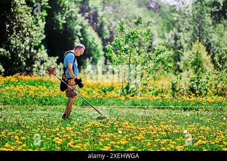 L'agricoltore utilizza un gancio per zaino quando lavora con un rifinitore wacker a filo alimentato a gas. Foto Stock