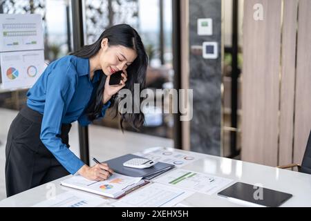 BeautifulÂ donna segretaria asiatica fiduciosa intelligente donna d'affari professionale Â parlare su phoneÂ Â a officeà¹ƒ Foto Stock