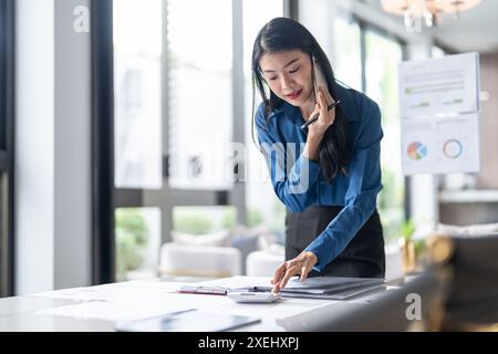 BeautifulÂ donna segretaria asiatica fiduciosa intelligente donna d'affari professionale Â parlare su phoneÂ Â a officeà¹ƒ Foto Stock