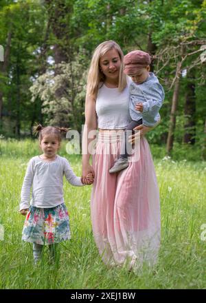 La famiglia cammina nel parco. Mamma tiene il suo figlio tra le braccia. D'altra parte, una figlia piccola. Madre di famiglia e figli. La gioia di Mothe Foto Stock