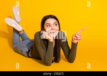 Foto a tutta lunghezza di una bella signora adolescente che sdraiata sul pavimento sembra uno spazio vuoto vestito elegante indumento cachi isolato su sfondo giallo Foto Stock