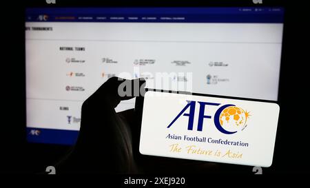 Persona che possiede un telefono cellulare con il logo dell'associazione Asian Football Confederation (AFC) di fronte alla pagina web. Mettere a fuoco il display del telefono. Foto Stock