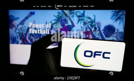 Persona con smartphone con logo dell'associazione Oceania Football Confederation (OFC) davanti al sito web. Mettere a fuoco il display del telefono. Foto Stock