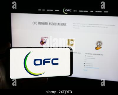 Persona che possiede un telefono cellulare con il logo dell'associazione Oceania Football Confederation (OFC) davanti alla pagina web. Mettere a fuoco il display del telefono. Foto Stock