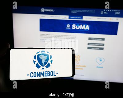 Persona con smartphone con logo Confederacion Sudamericana de Futbol (CONMEBOL) davanti al sito web. Mettere a fuoco il display del telefono. Foto Stock