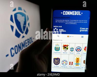 Persona che detiene un telefono cellulare con il sito web della Confederacion Sudamericana de Futbol (CONMEBOL) davanti al logo. Messa a fuoco al centro del display del telefono. Foto Stock