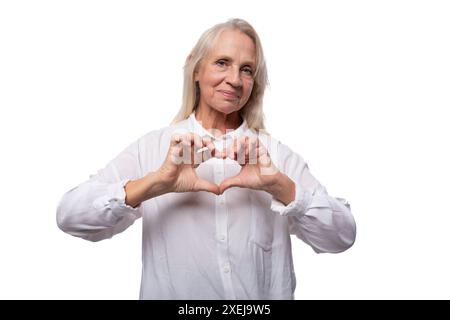 Un'anziana donna d'affari con i capelli grigi in camicia mostra un cuore Foto Stock