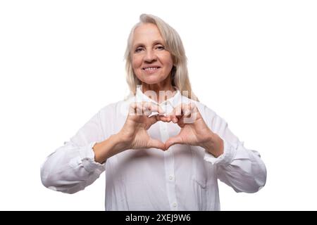 Ritratto di una donna d'affari anziana con i capelli grigi in una camicia che mostra un cuore con le mani Foto Stock