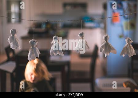 Piccole decorazioni fantasma appese su una corda al chiuso con un bambino Foto Stock