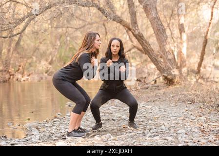 Donne che si allenano vicino a un fiume che accovacciano Foto Stock