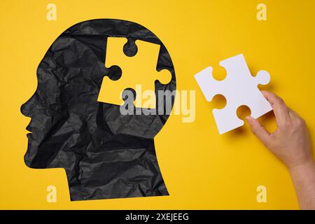 Silhouette di una testa umana che regge un pezzo di puzzle su uno sfondo giallo, che rappresenta la salute mentale Foto Stock