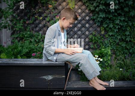 ragazzo in tuta che si gode un libro in natura con luce dorata Foto Stock