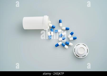 Capsule blu e bianche fuoriuscite da un vaso medicinali su sfondo blu. Foto Stock